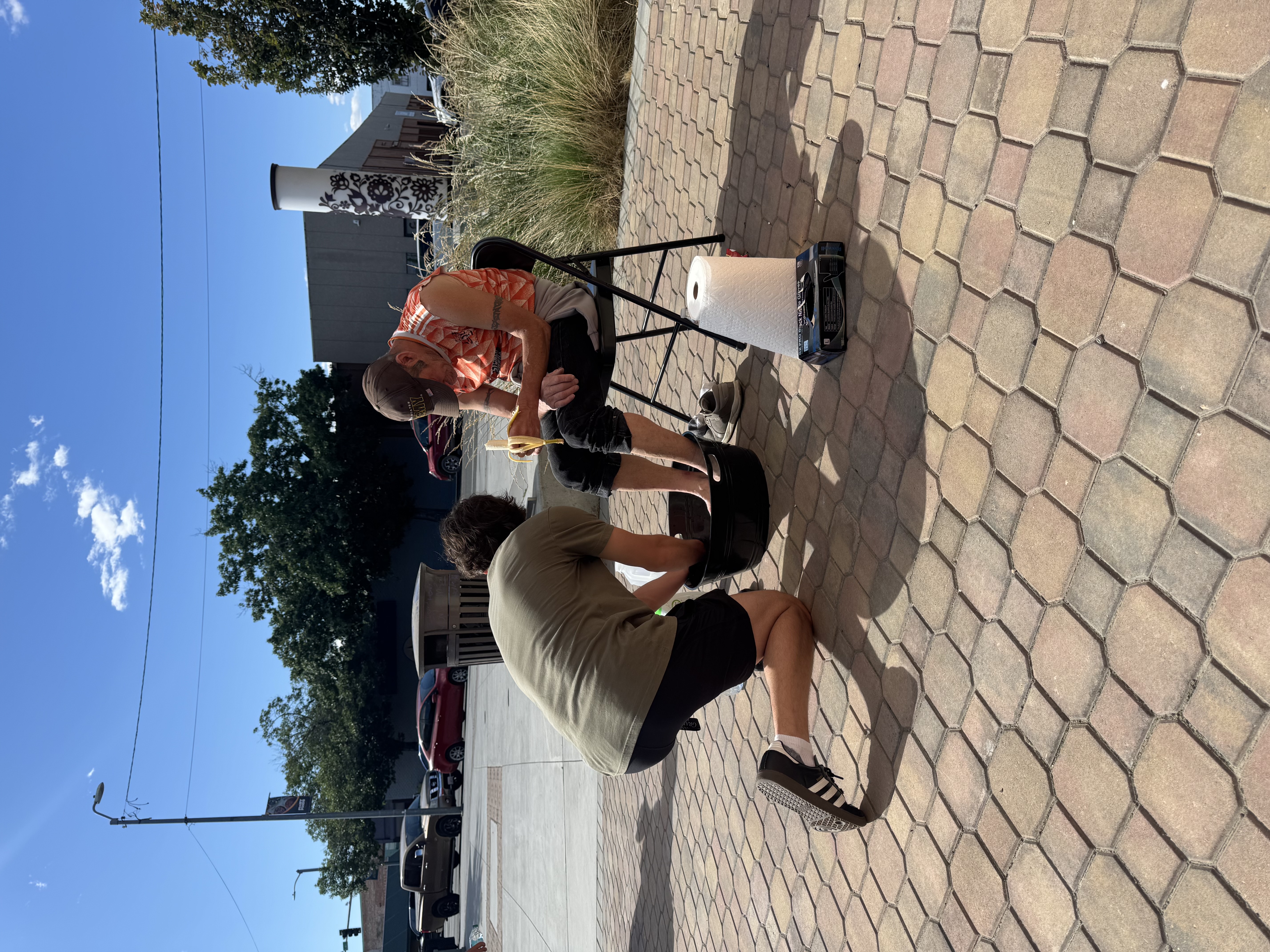 A volunteer kneeling to wash someone's feet on the street